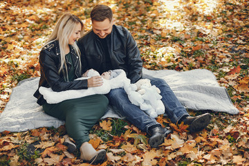 Family in a autumn park. Woman in a black jacket. Cute newborn little girl with parents