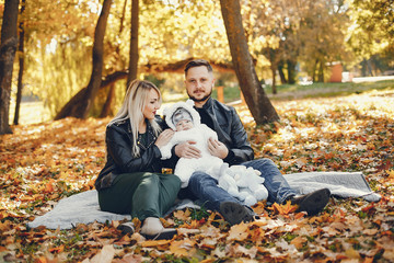 Fototapeta premium Family in a autumn park. Woman in a black jacket. Cute newborn little girl with parents
