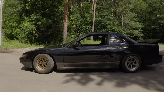 Black drift s13 car standing on countryside road on summer forest background. Old japanese car parking on roadside suburban highway at sunny day