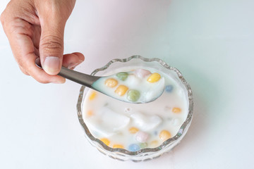 Hand holding spoon to scooping rice balls with young coconut in sweet coconut milk in a cup isolated on white  tile background Thai people call Bua Loi.