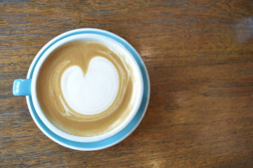 Top view of latte with milk foam art in blue cup on wooden table, caffeine concept.