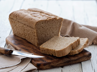 Fresh homemade bread, partially sliced. Bread is located on a wooden surface. Near napkins and a knife. White wood background. Close-up. The concept for baking.
