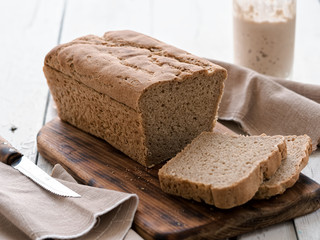 Fresh homemade bread, partially sliced. Bread is located on a wooden surface. Near napkins and a knife. Jar with yeast. White wood background. Close-up. The concept for baking.