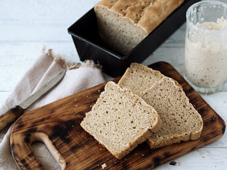 Fresh homemade bread, partially sliced. Bread is located on a wooden surface. Near napkins and a knife. Jar with yeast. White wood background. Close-up. The concept for baking.