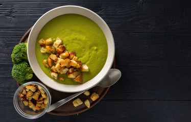 Bowl of cream broccoli soup with bread croutons on a wooden background
