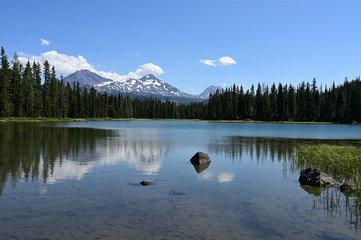 Fototapeta na wymiar Middle and North Sisters volcanoes reflected in the still water of Scott Lake on a clear and sunny summer afternoon.