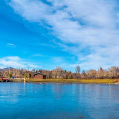 Fototapeta premium Square Winter view of an icy lake reflecting the radiant blue sky with clouds