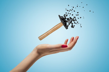 Female hand holding small hammer shattering into pieces on blue background