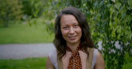 Portrait of a pretty positive Asian girl on the background of a green Bush in the Park