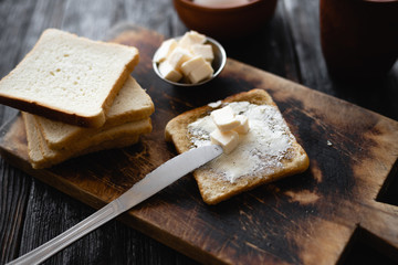 kitchen table, a piece of bread on the table, a toast with a crust and butter, a knife and a cutting board