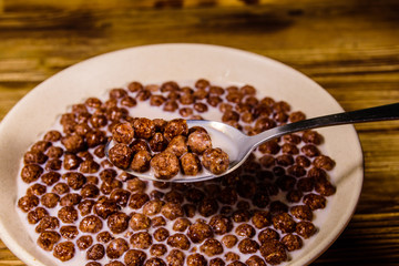 Ceramic plate with chocolate cereal balls in milk on wooden table