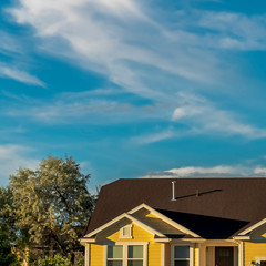 Square frame Home exterior with dark roof and cream wall viewed against sunny cloudy blue sky