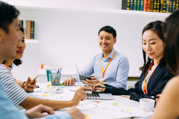 Asian mature business man smiling and looking at camera while sitting in meeting with other...