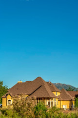 Fototapeta na wymiar Home with brown roof and yellow wall against mountain and clear blue sky