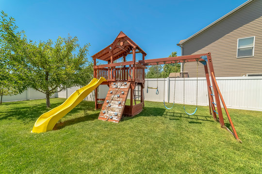 Wooden playground structure with yellow plastic slide swings and climbing wall