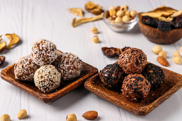 Healthy energy balls of nuts, oatmeals and dried fruit with coconut, flax and sesame seeds on wooden coconut plates on a white background, horizontal orientation