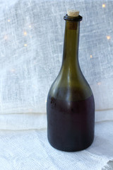 an old misted bottle of wine is closed by a cork against a background of light drapery with lights. holiday still life
