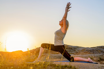 Young woman doing yoga on top of a mountain at sunset, free space.