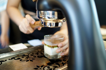 Coffee machine pours espresso to glass of iced matcha green tea with milk, Refreshing Summer Drink.