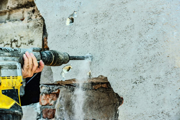 A man with a jackhammer makes an opening in the wall.