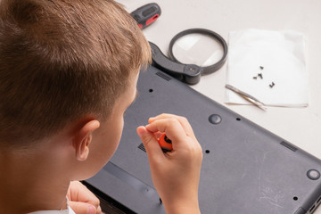 A boy of 10 years old is sorting a laptop for cleaning and maintenance. Selective focus. Screwdrivers, purge cylinder, magnifying glass and spray cleaner in the frame.