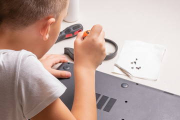 A boy of 10 years old is sorting a laptop for cleaning and maintenance. Selective focus. Screwdrivers, purge cylinder, magnifying glass and spray cleaner in the frame.