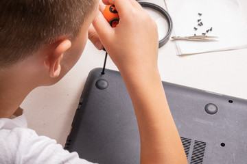 A boy of 10 years old is sorting a laptop for cleaning and maintenance. Selective focus. Screwdrivers, purge cylinder, magnifying glass and spray cleaner in the frame.