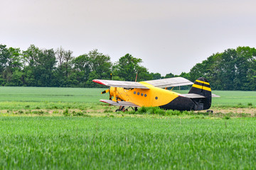 Fototapeta na wymiar Yellow plane on a wheat field. Sowing, reaping, fertilizer of agricultural crops.