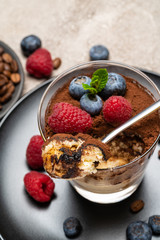 Classic tiramisu dessert portion with blueberries and raspberries in a glass cup on concrete background