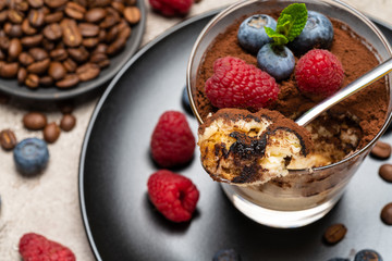Classic tiramisu dessert portion with blueberries and raspberries in a glass cup on concrete background