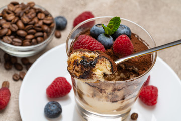Classic tiramisu dessert portion with blueberries and raspberries in a glass cup on concrete background