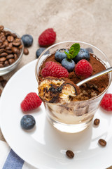 Classic tiramisu dessert portion with blueberries and raspberries in a glass cup on concrete background