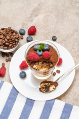 Classic tiramisu dessert portion with blueberries and raspberries in a glass cup on concrete background