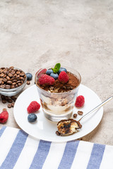Classic tiramisu dessert portion with blueberries and raspberries in a glass cup on concrete background