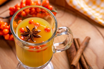 Hot beverage of sea-buckthorn berries in glass cup on wooden background. Rustic style.