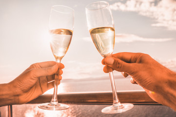 Luxury cruise ship travel couple toasting champagne glasses for celebration honeymoon. Caribbean holiday drinking doing cheers at sunset view sun flare of cruise holiday destination.