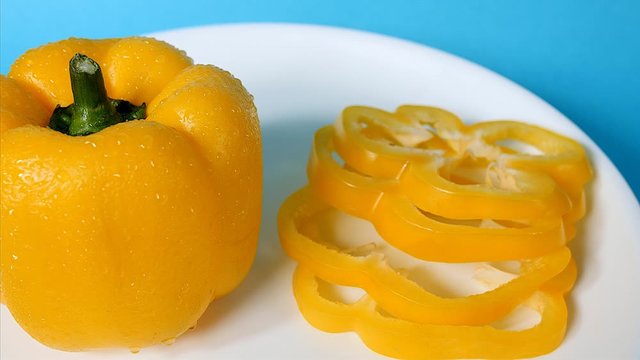 Close of shot of a sliced and one whole yellow capsicum on a white plate. 