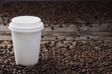 White takeaway cup of coffee with beans on brown wooden table