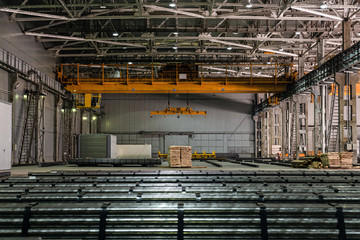 Yellow overhead crane in engineering plant shop. Industrial metalwork production hall and warehousing workshop of matal rods billets.