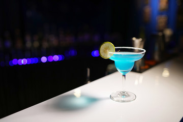 Holding a glass of blue margarita cocktail with salty rim and slice of lime on blurred background and copy space, The Bar counter in Nightclub.