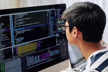 Fototapeta na wymiar Smart teenage boy in glasses checking programming code on computer screen when sitting at his desk