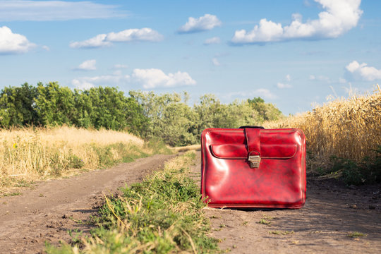 Suitcase on the road between a wheat field. Travel, vacation concept