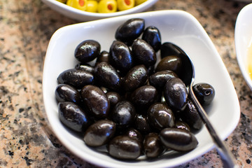 White ceramic bowl filled with marinated black olives. Olives from Turkey.