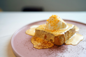 A plate of french toast (pain perdu) with salted yolk egg sauce, topped with vanilla ice cream and egg yolk flakes on marble table and blurred background.