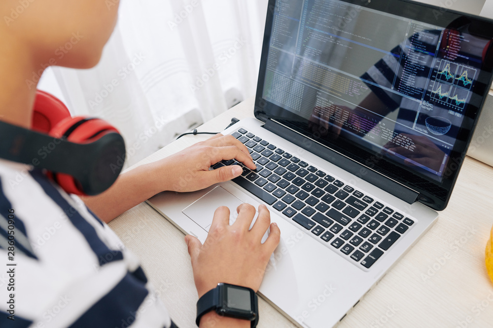 Wall mural teenage boy with smartwatch and heaphones programming on laptop, he is testing new software he creat