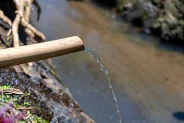 Water from the bamboo tube flows into the river in Ubud, Island Bali, Indonesia. Closeup