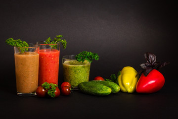 Still life. Vegetable juices in glass glasses, tomatoes, yellow pepper, cucumbers, green and purple basil leaves, parsley on a black background. Close-up. Isolated. Vegetarianism.