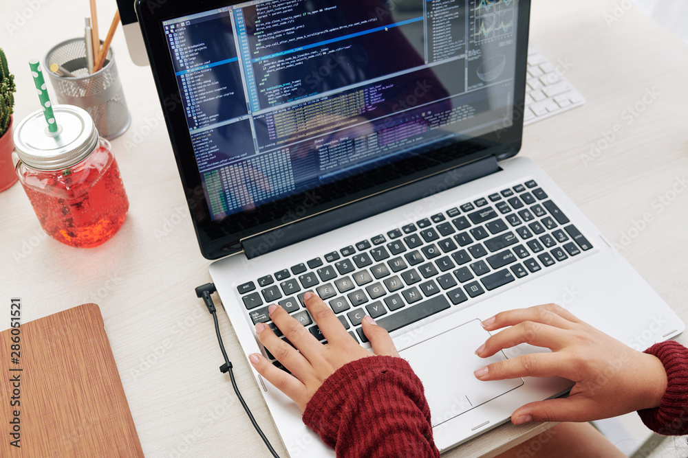 Wall mural hands of girl programming or testing new software on her laptop, view from above