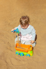 Baby girl boy playing in the sand with a toy car. Sand pours from a shovel into a car body