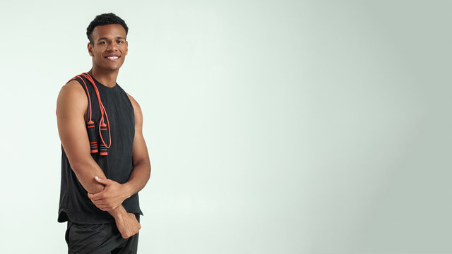 Way of my life. Positive young afro american man holding a jumping rope at his shoulders and smiling while standing against grey background